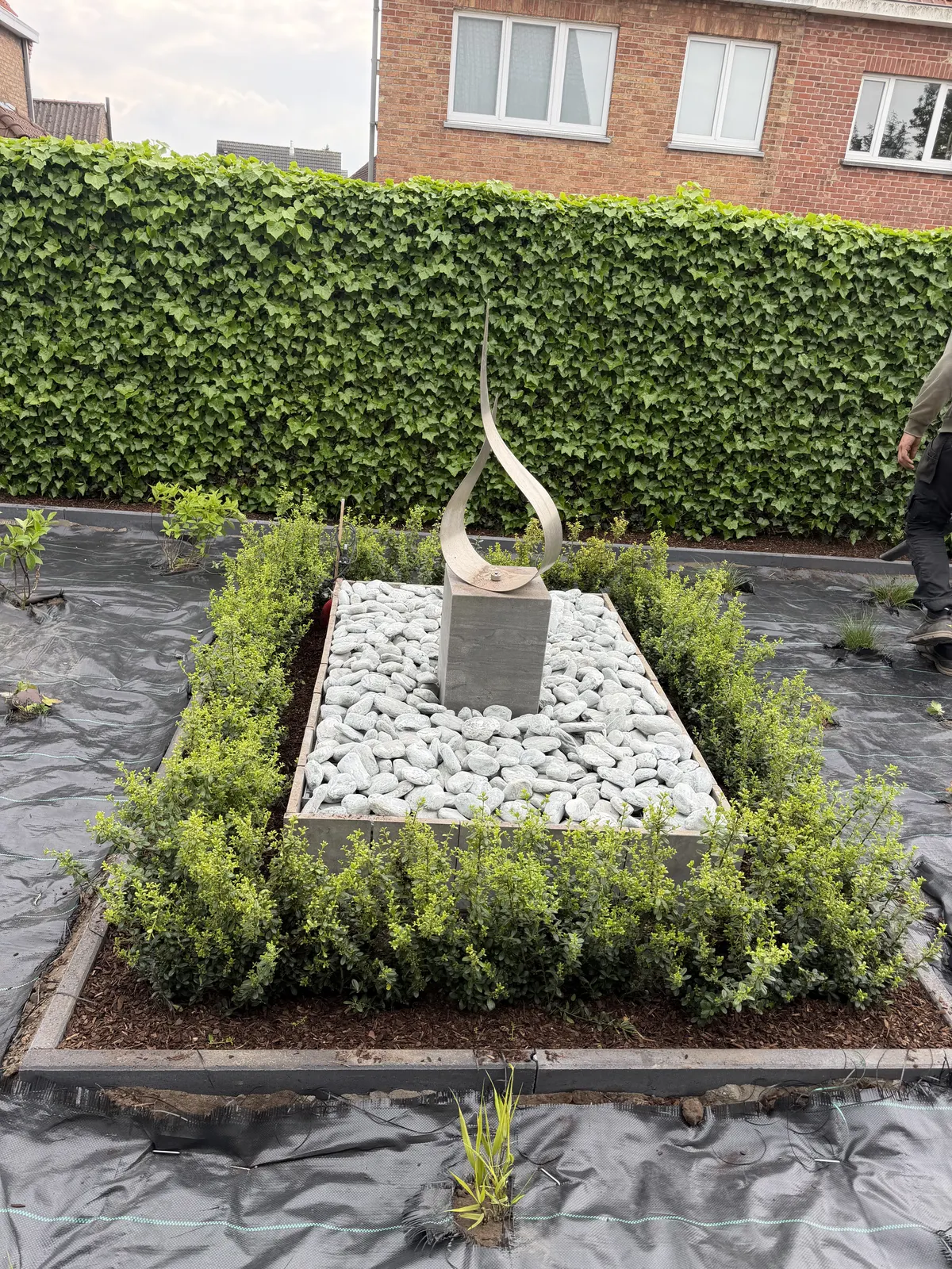 Nieuwe beplanting met witte kiezels en sculptuur in een voortuin