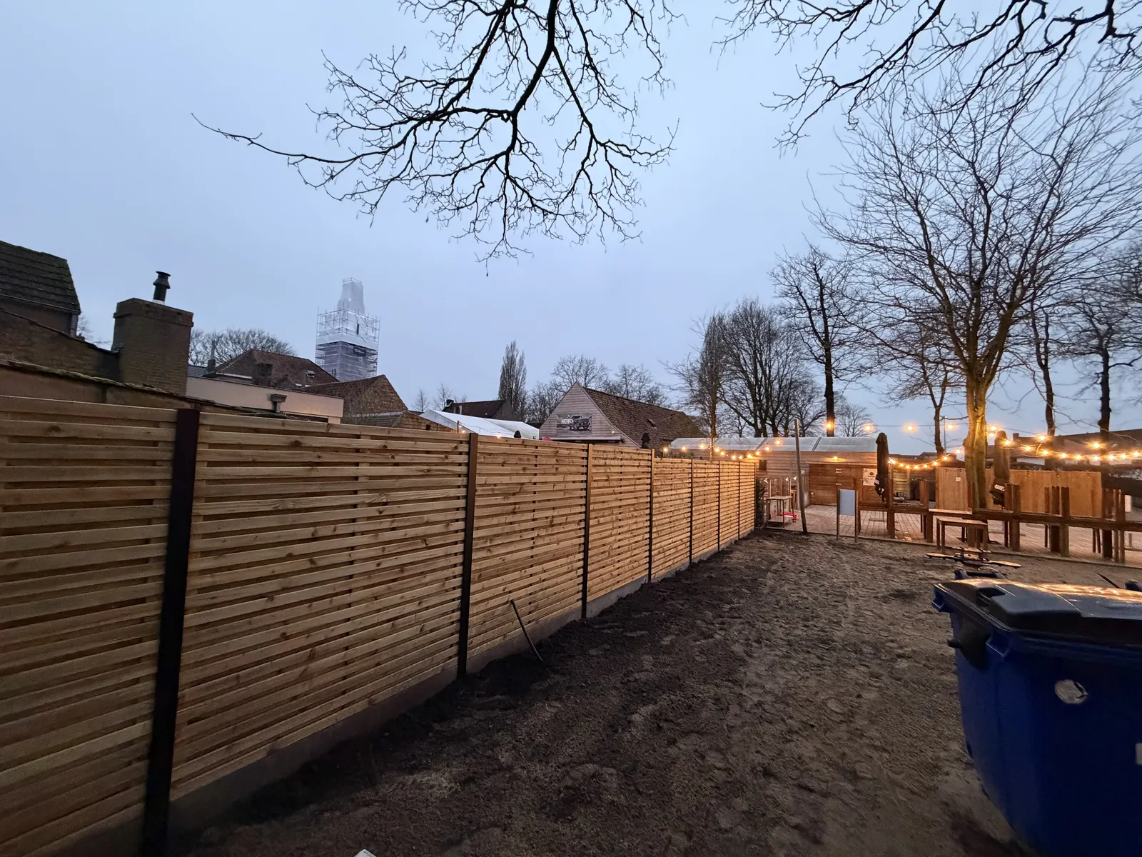 Houten omheining met betonpalen in een tuin met sfeerverlichting