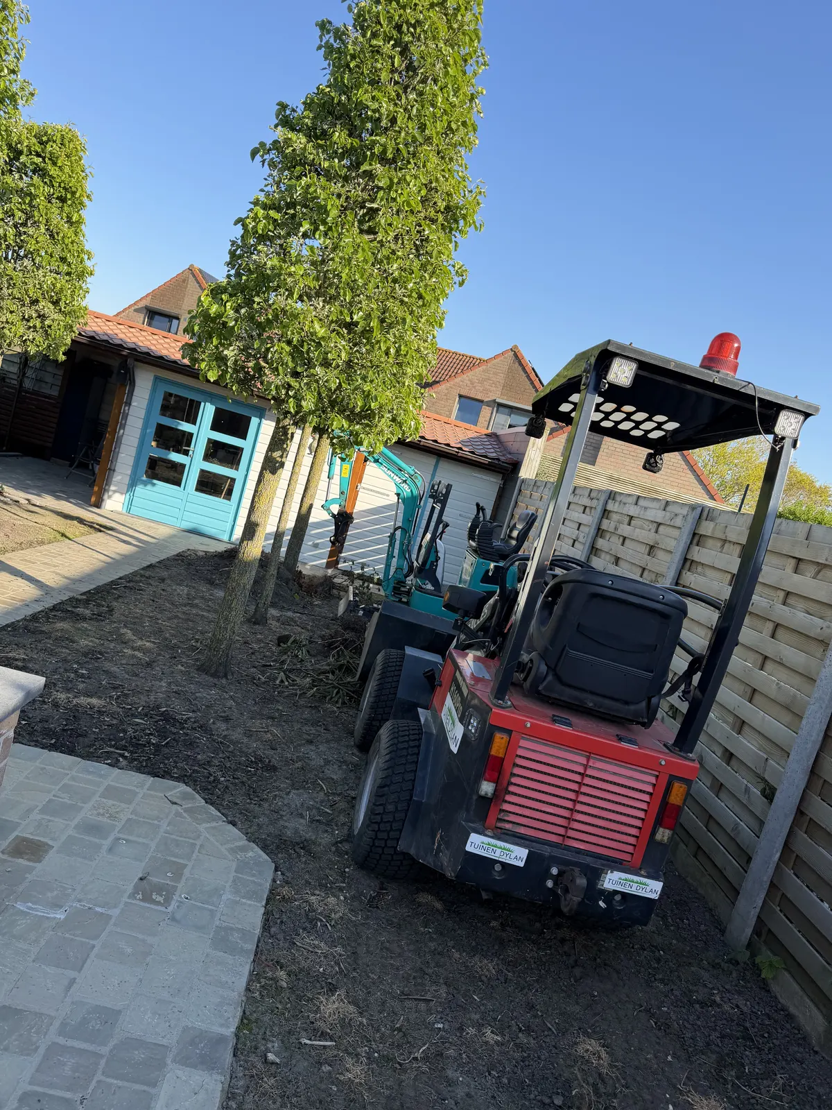 Minigraver en kraanwagen aan het werk tijdens een tuinaanleg