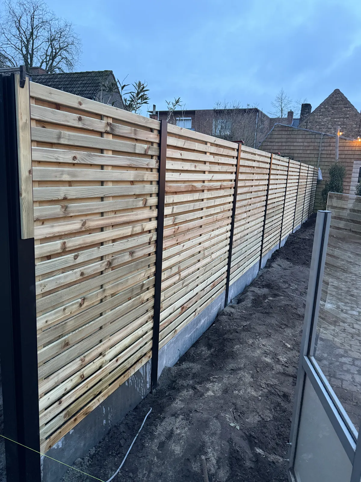 Moderne houten omheining met zwarte palen naast een glazen balustrade