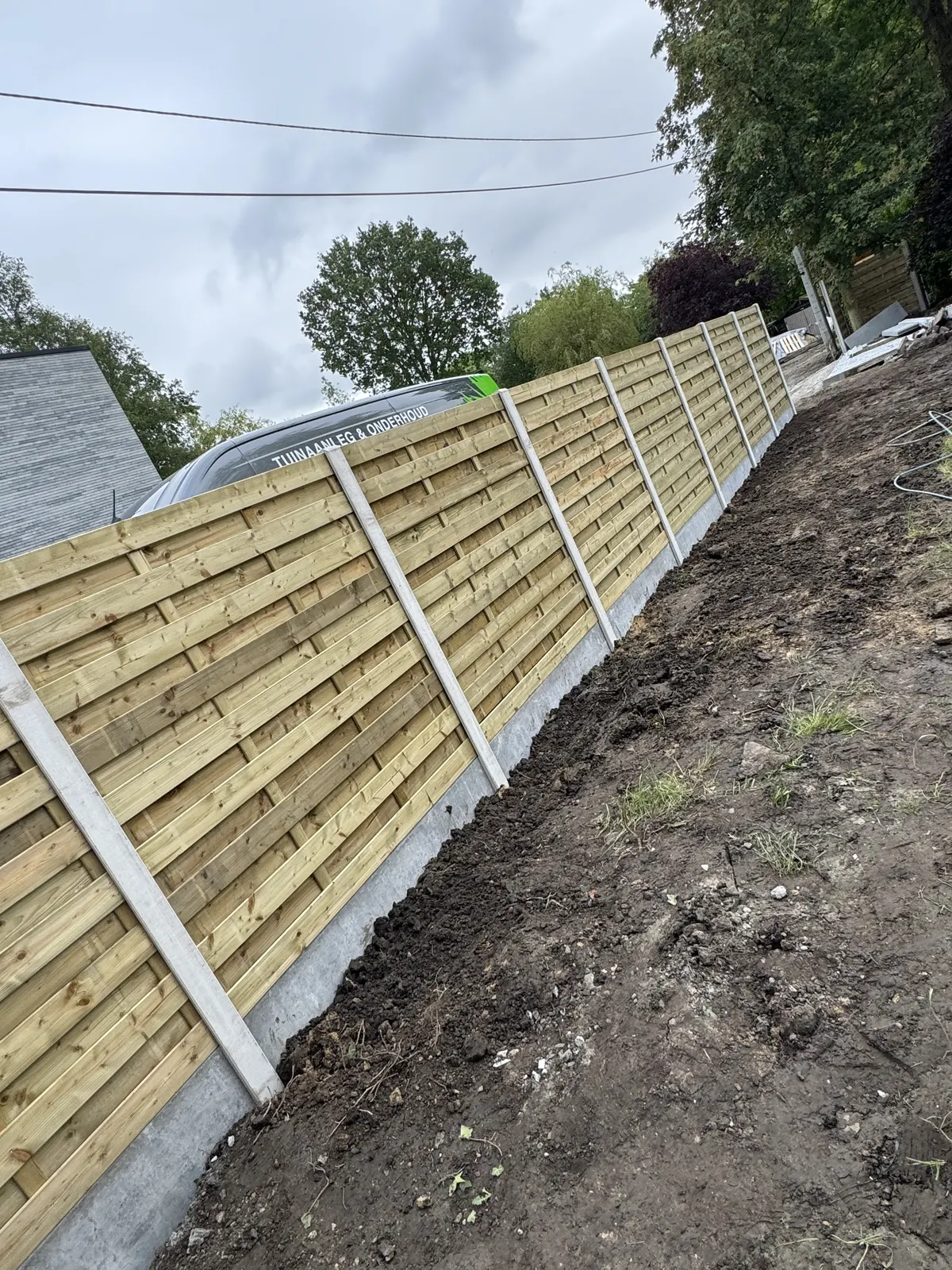 Houten omheining met betonpalen geplaatst op een hellend terrein