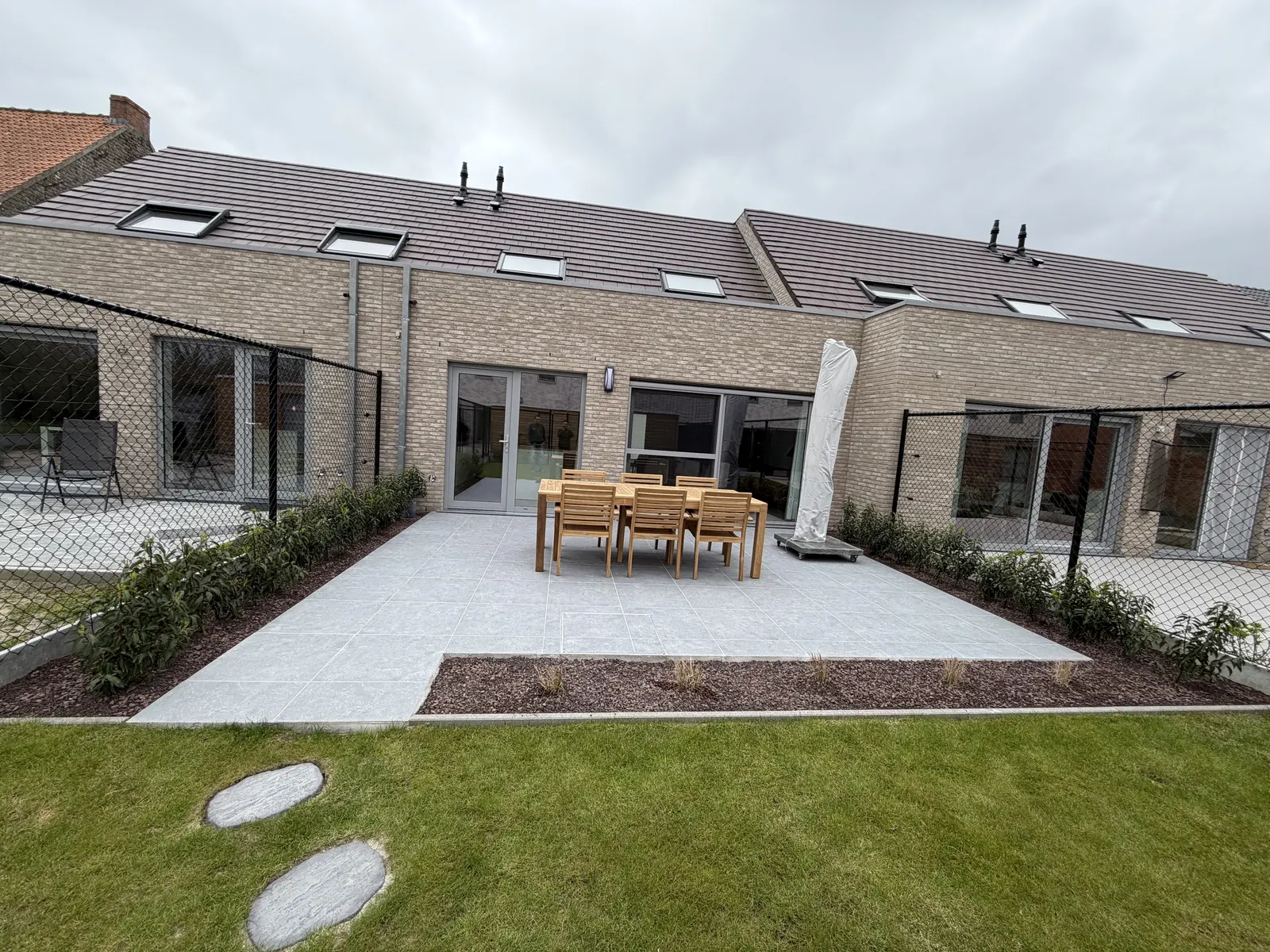 Terras in keramische tegels met tuinset naast een nieuw gazon